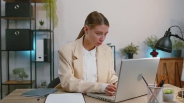 Businesswoman working on laptop computer smiling friendly at camera and waving hands gesturing hello, hi, greeting or goodbye, welcoming with hospitable expression to colleague at office workplace