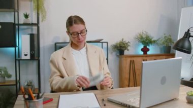 Rich happy businesswoman in suit counting money cash, calculate financial bills use laptop computer working at office workplace desk. Freelance woman satisfied of income earnings, profit. Girl worker