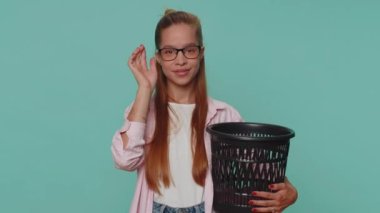 Pretty teenager young girl taking off, throwing out glasses into bin after vision laser treatment therapy, looking smiling at camera. Student child kid isolated on blue studio background indoors