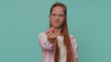 Aggressive angry pretty teenager girl in shirt trying to fight at camera, shaking fist, boxing with expression, punishment. Young teen female child kid isolated alone on blue studio background indoors
