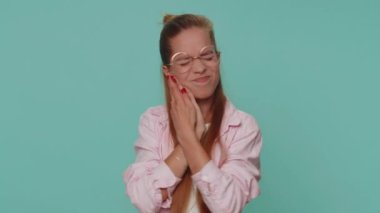 Dental problems. Pretty teen young girl touching cheek, closing eyes with expression of terrible suffer from painful toothache, sensitive teeth, cavities. Student child kid on blue background indoors