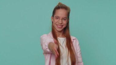 Friendly pretty teenager young girl outstretching hand to camera, offering handshake, greeting with kind smile, welcoming showing solidarity, trust concept. Student child kid on blue studio background