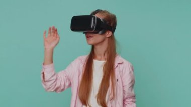 Excited teenager young girl using headset helmet app to play simulation game. Watching virtual reality 3D 360 video. Student child kid in VR goggles device isolated on blue studio background indoors
