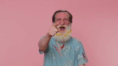 Amused senior man flowered beard pointing finger to camera, laughing out loud taunting making fun of ridiculous appearance, funny joke. Elderly grandfather posing alone on pink studio wall background