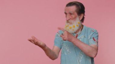 Handsome senior man showing thumbs up and pointing empty place, advertising area for commercial text, copy space for goods promotion. Elderly grandfather. Studio shot indoors on pink wall background