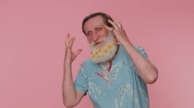 Funny joyful sincere mature man 60 years old making playful silly facial expressions and grimacing, fooling around showing tongue. Senior handsome grandfather isolated alone on pink wall background