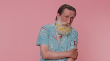 Smiling playful happy senior man with flowers in gray-haired beard blinking eye, looking at camera with toothy smile, winking and flirting, expressing optimism. Elderly grandfather on pink background