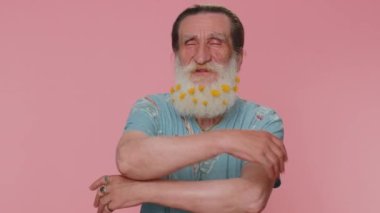 Come to me, I want to embrace you. Senior man with flowers in beard spread hands and give hug to you. Pleasant expression, love feelings. Elderly grandfather isolated alone on pink studio background