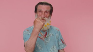 Aggressive angry senior bearded man trying to fight at camera, shaking fist, boxing with expression, punishment, disappointment. Elderly grandfather isolated alone on pink studio wall background