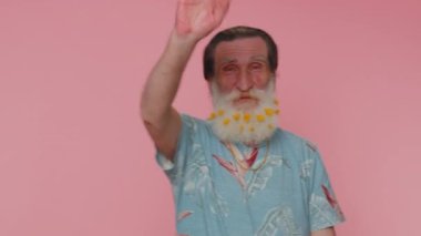 Handsome senior beard old man smiling friendly at camera and waving hands gesturing hello or goodbye, welcoming with hospitable expression. Happy grandfather indoors isolated on pink wall background