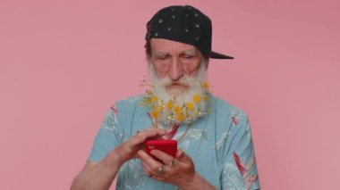 Mature man flowered beard using mobile phone typing new post on web sms message, browsing, searching addiction of social networks. Senior grandfather studio shot isolated alone on pink background