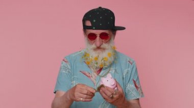 Poor man upset over insufficient amount of money holding piggybank and one dollar banknote. Financial crisis. Bankruptcy. Poverty and destitution. Senior grandfather isolated on pink studio background