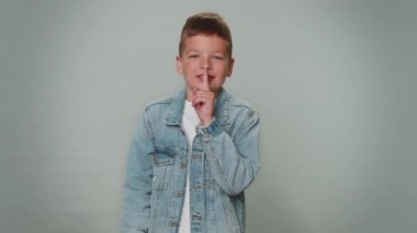 Shh be quiet please. Portrait of toddler boy 10 years old presses index finger to lips makes silence gesture sign do not tells secret. Young beautiful children teenager child on gray studio background