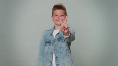 Toddler boy showing victory sign, hoping for success and win, doing peace gesture, smiling with kind optimistic expression. Young teenager children child kid indoor isolated on gray studio background