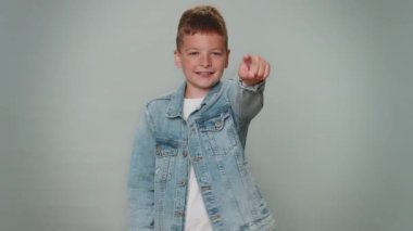 Call me, here is contact number. Toddler boy in jeans jacket looking at camera doing phone gesture like says hey you call me back. Young teenager schoolboy child kid isolated on gray wall background