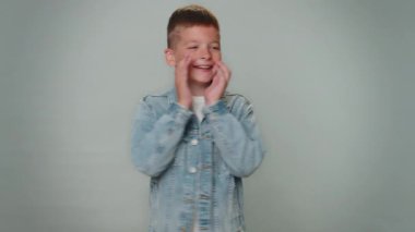 Expressive toddler kid boy holding hands near mouth loudly screaming, shouting, yelling, announces discounts sale Hurry up, welcomes someone hello. Young teenager child schoolboy on gray background