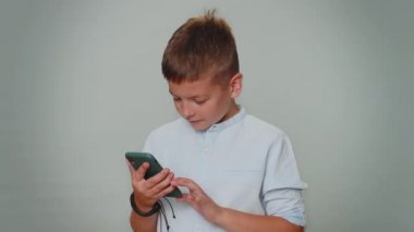 Happy excited joyful child boy use mobile cell phone typing browsing shouting say wow yes found out great big win, good news, lottery goal achievemen, celebrating success, winning on gray background