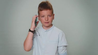 Toddler kid boy in shirt having pleasant mobile conversation using smartphone with friends or family, telling good news. Young teenager child schoolboy isolated alone on gray studio background indoors