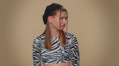 Cheerful funny bully young woman in crop top. Adult girl showing tongue making faces at camera, fooling around, joking, aping with silly face, teasing isolated alone on beige studio background indoors
