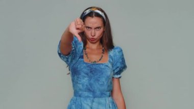 Upset lovely pretty young woman showing thumbs down sign gesture, expressing discontent, disapproval, dissatisfied, dislike. Adult stylish female girl isolated alone on gray studio background indoors