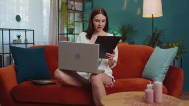 Girl accountant working with financial graph documents, calculate taxes for charts and graph reports of home income on couch. Young businesswoman working on laptop computer, planning expenses budget