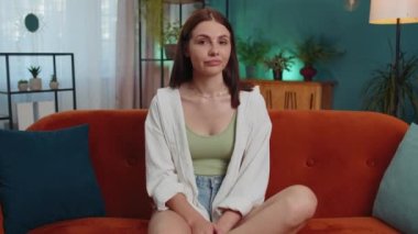Displeased upset female girl reacting to unpleasant awful idea, dissatisfied with bad quality, wave hand, shake head No, dismiss idea, dont like proposal at home. Young woman sitting on orange sofa