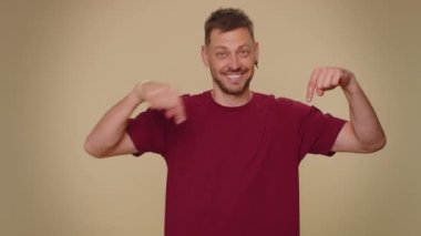 Look at advertisement. Bearded handsome young man pointing down, saying to subscribe, gesturing ok and like, showing place for commercial, promotional information below. Adult guy on beige background