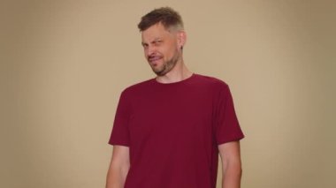 Dont want to look at this, awful. Handsome young man closing eyes with hand showing stop gesture, confused shy scared to watch. Adult stylish male guy isolated on beige studio wall background indoors