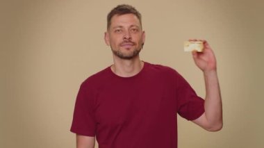 Happy man showing plastic credit bank card advertising transferring money cashless, purchases online shopping, sale discount, internet order delivery purchase. Adult stylish guy on beige background