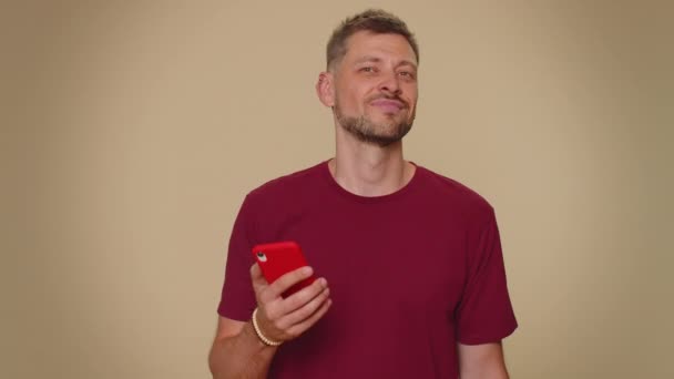Счастливый Молодой Человек Красной Футболке Выглядящий Смартфоном Искренне Радуется Победе — стоковое видео