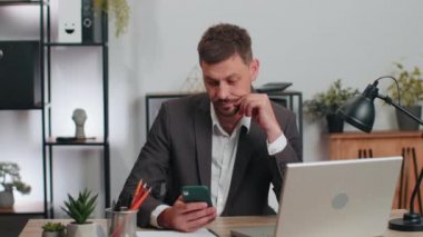 Business man programmer software developer in suit working at office finishing up phone call selling online using smartphone making victory gesture, receiving good news rejoicing over success triumph