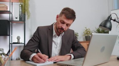 Businessman lawyer in suit working on laptop computer online, writing notes in planner notebook at office workplace desk. Professional freelancer student man. Remote education, study, learning lessons