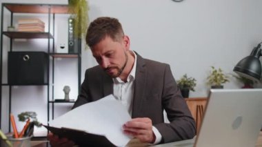 Oh my God, Wow. Businessman in suit working analysing paperwork documents raising hands in surprise, shocked by sudden victory, good news at home office desk. Confident male manager freelancer man