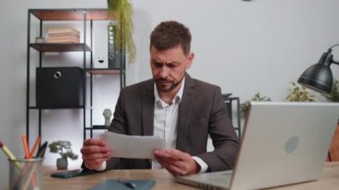 Stressed businessman in suit working looking at unpaid bank debt bills, doing paperwork, planning budget, calculate finances mortgage payments at office. Displeased freelancer man throws paper bills