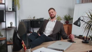 Cheers. Businessman drinking champagne from glass after working, putting legs on table sitting at office. Happy male manager freelance man relaxing and celebrate successful contract win agreement