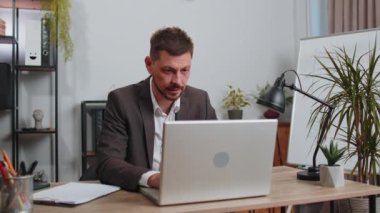 Happy businessman in suit working on laptop computer sincerely rejoicing win, receiving money dollar cash banknotes, success lottery luck at office workplace desk. Professional manager freelancer man