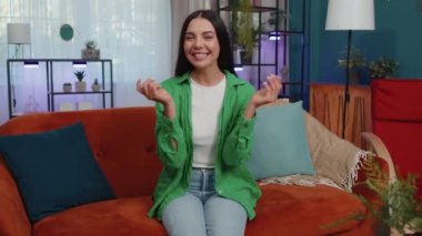 Portrait of caucasian cheerful rich girl showing wasting or throwing money around hand gesture, more tips earnings, big profit, win lottery, body language, share. Young woman at home in room on couch
