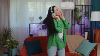 Happy relaxed overjoyed woman in wireless headphones dancing at home choosing listening favorite energetic disco rock n roll music in smartphone app. People weekend activities. Funny joyful girl