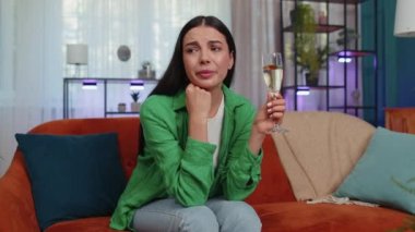 Sad young woman looks pensive of unrequited love, suffers from unfair situation, drinking champagne. Problem, break up, depressed feeling bad annoyed, burnout, bankruptcy. Girl sitting at home room