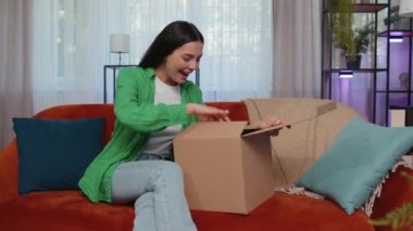 Portrait of happy girl unpacking delivery parcel sitting at home. Smiling satisfied young woman shopper, online shop customer opening cardboard box receiving purchase gift by fast postal shipping