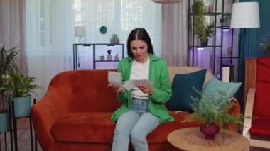 Stressed girl at home room looking at unpaid bank debt bills, doing paperwork, planning budget, calculate finances mortgage payments. Displeased young woman throws paper bills sitting on orange couch