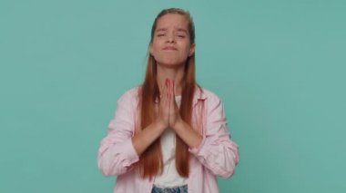Please, God help. Teenager young girl praying, looking upward and making wish, asking with hopeful imploring expression, begging apology. Student child kid isolated on blue studio background indoors