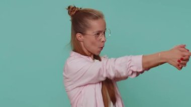 Pretty teenager girl pointing around with finger gun gesture, looking confident, making choice, shooting killing with hand pistol right on target. Young child kid isolated on blue studio background