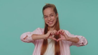 I love you. Smiling lovely pretty teenager girl makes heart gesture demonstrates love sign expresses good feelings and sympathy. Young teen female child kid isolated on blue studio background indoors