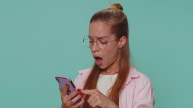 Sad teenager student girl in glasses use smartphone typing browsing, loses becoming surprised sudden lottery results, bad fortune, loss. Young child kid isolated on blue studio background indoors