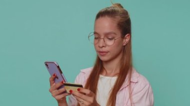 Happy teenager girl use smartphone, plastic credit bank card, browsing say wow yes, found out great big win, success lotter, good news, purchases online shopping. Child kid on blue studio background