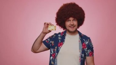 Happy tourist man showing plastic credit bank card advertising transferring money cashless, purchases online shopping, sale discount, internet order delivery purchase. Young guy boy on pink background