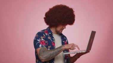 Happy tourist man working online on laptop, finishing work, showing thumb up to camera, positive feedback, like, lottery win, approve good offer advertisement. Young bearded guy boy on blue background