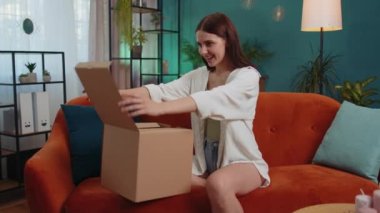 Portrait of happy girl unpacking delivery parcel sitting at home. Smiling satisfied young woman shopper, online shop customer opening cardboard box receiving purchase gift by fast postal shipping