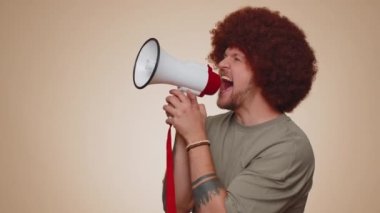 Smiling happy bearded man talking with megaphone, proclaiming news, loudly announcing sale advertisement, warning using loudspeaker to shout speech. Young handsome adult guy on beige studio background